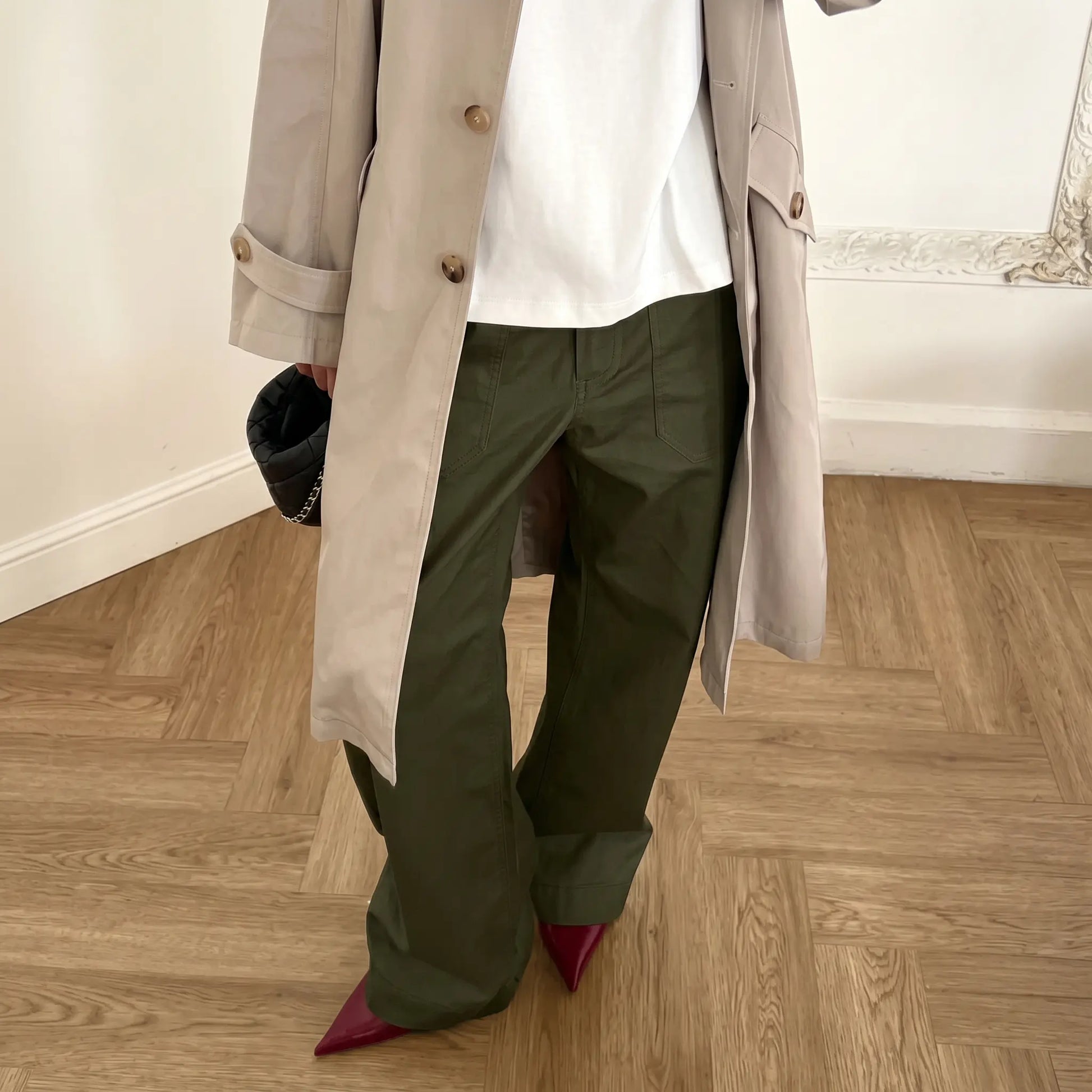 Olive green wide-leg utility trousers worn by a model in a styled outfit featuring a trench coat and heels, showcasing the relaxed fit and front patch pockets.