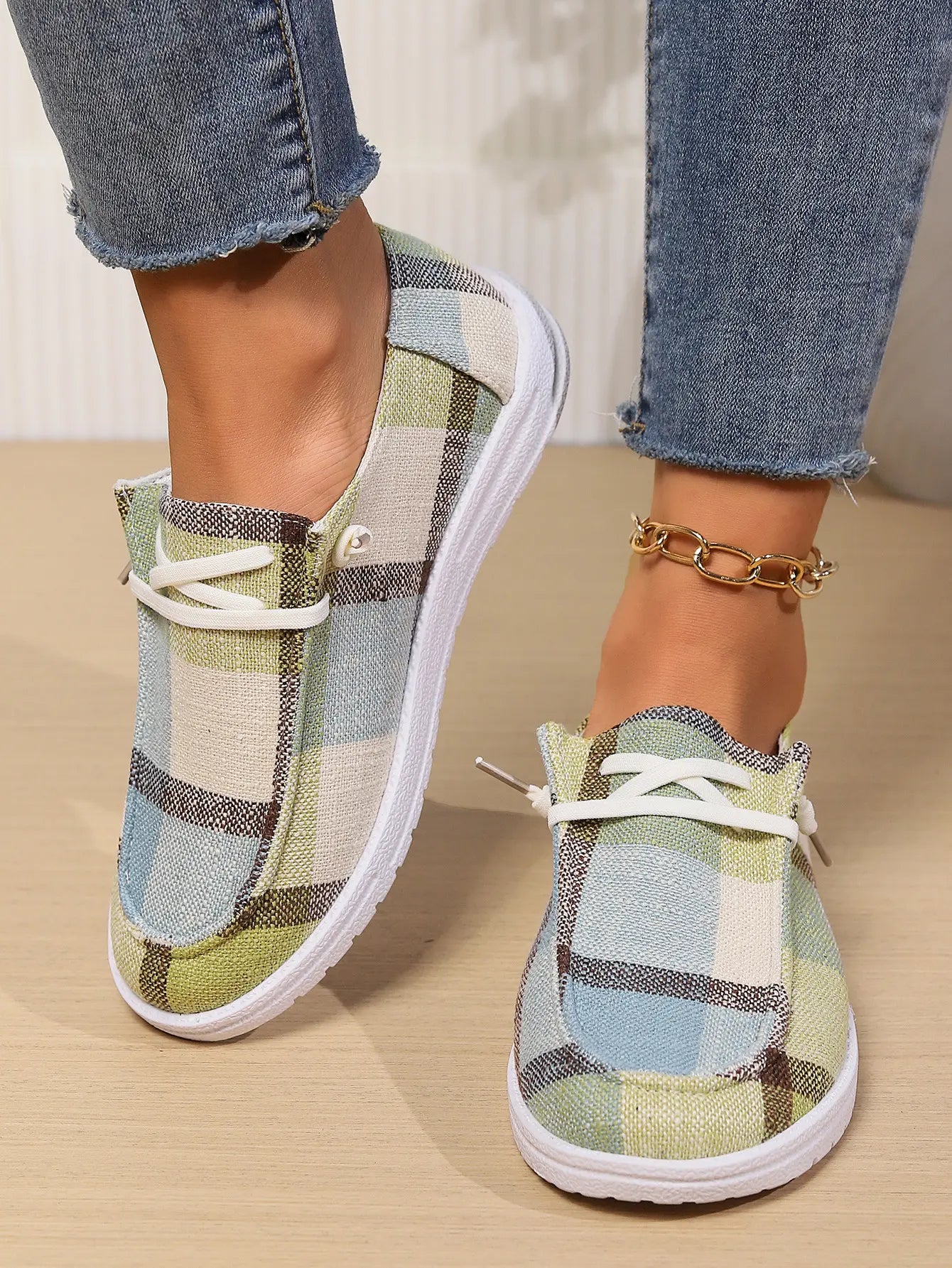 Lifestyle shot of Kaelen comfortable canvas loafers worn by a model with cropped jeans, showcasing the earthy green, blue, and beige plaid pattern and white rubber sole.
