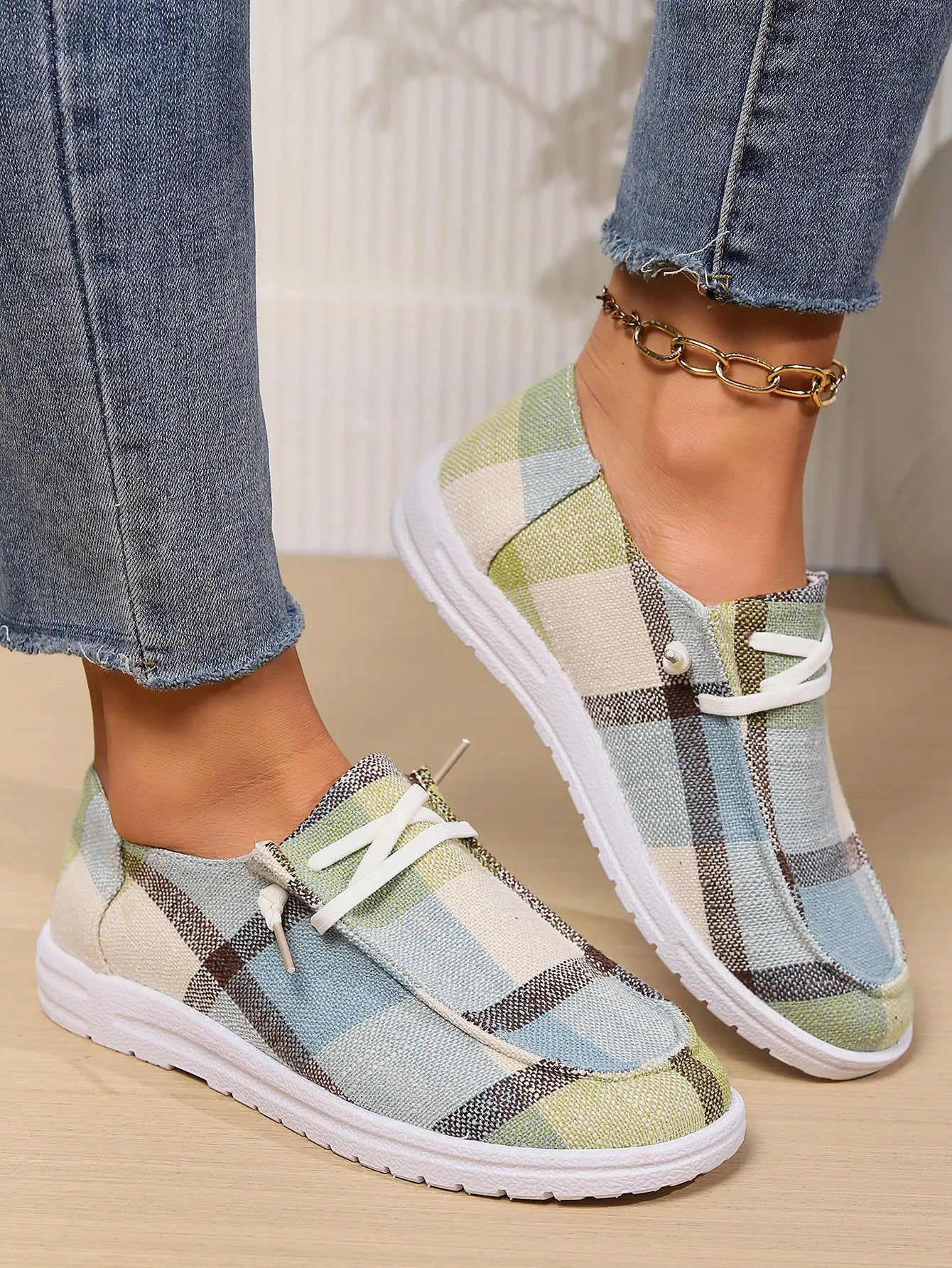 Kaelen comfortable canvas loafers with plaid pattern, featuring a blue, green, and beige woven textile, white laces, and a flat white rubber sole, worn on feet with jeans.
