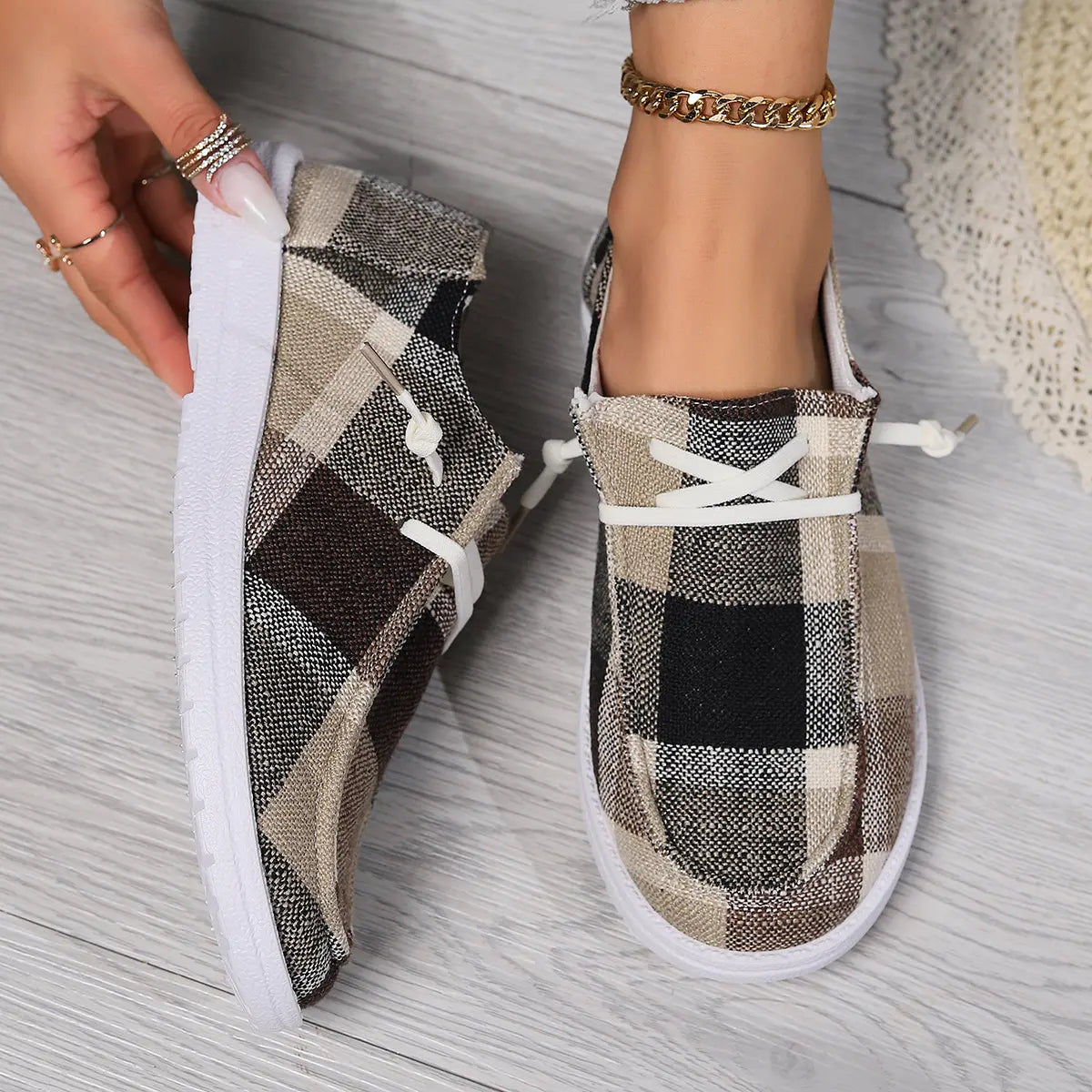 Close-up view of Kaelen plaid canvas loafers worn by a model, featuring round toes, white laces, and flexible white rubber soles on a light wood floor.