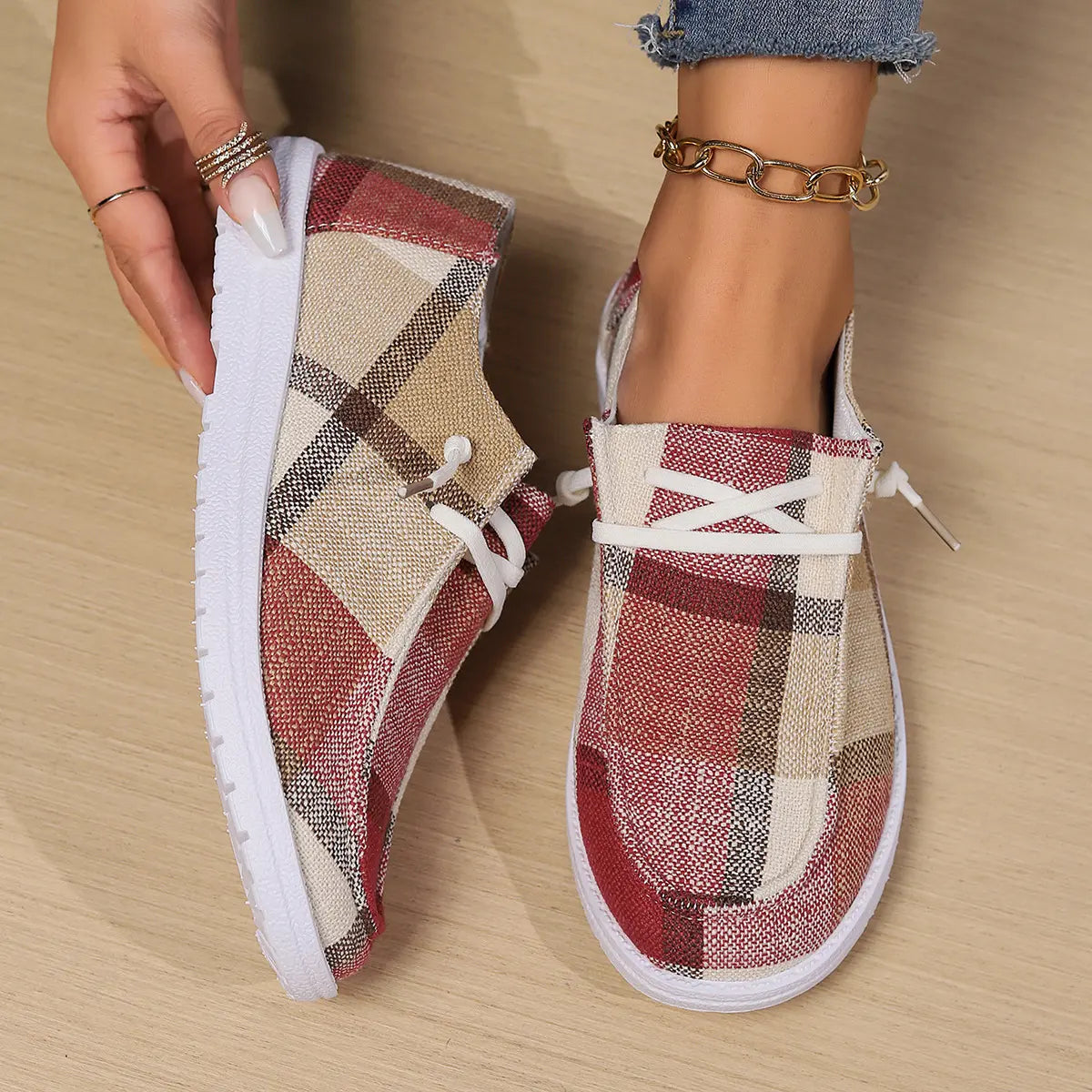 Kaelen plaid canvas slip-on loafers with decorative white laces and a white rubber sole, shown on a model's foot with a hand adjusting the shoe.