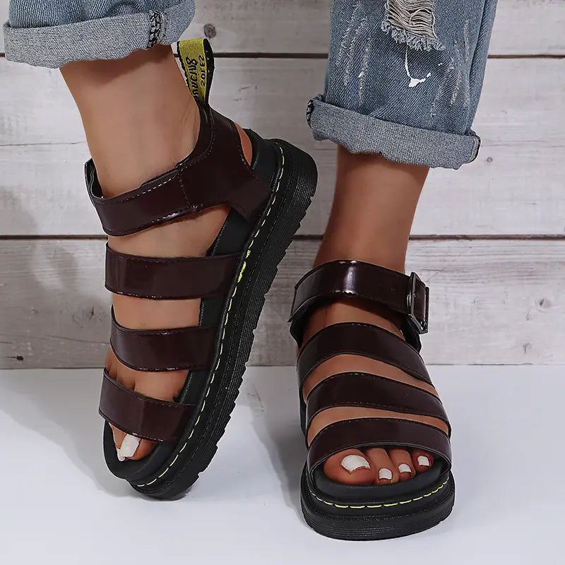 Platform gladiator sandals in a rich burgundy faux leather with a chunky black sole and black buckle strap, shown on a person's feet with cuffed denim jeans.