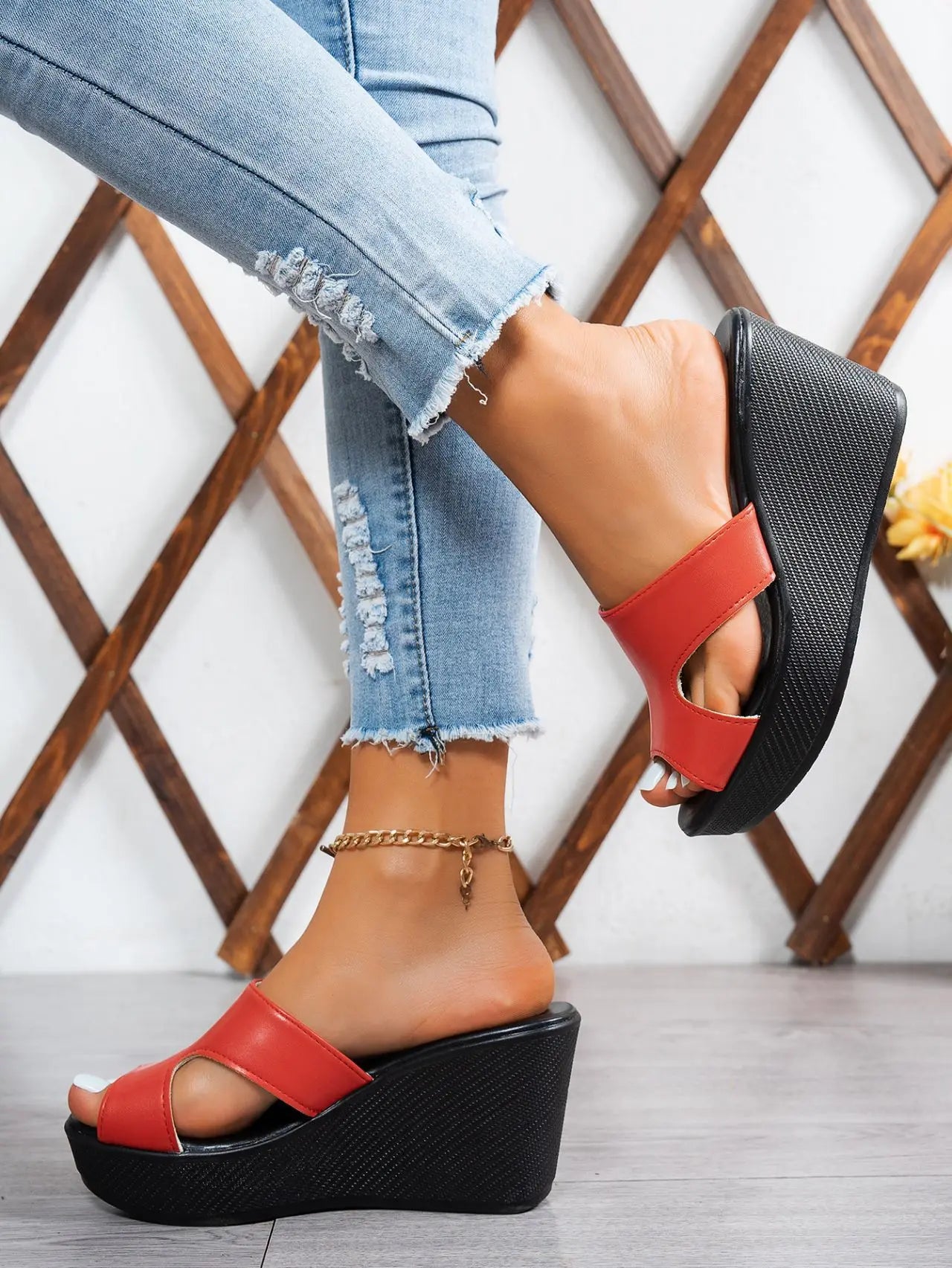 Kaelen red peep-toe wedge sandals styled with distressed denim jeans, showcasing the elegant single strap and stable platform heel on a woman's foot with an ankle bracelet.
