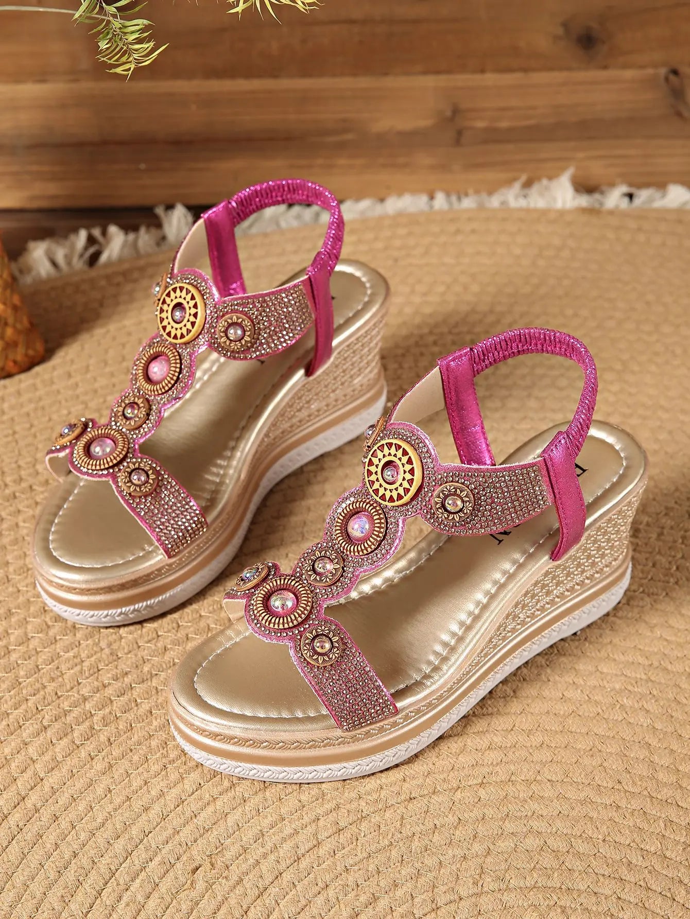 A pair of Kaelen embellished wedge sandals in shimmering rose gold with gold accents, featuring rhinestone and bead details on wavy straps and an elasticated slingback. The wedge sole has a woven espadrille-style texture and metallic band.