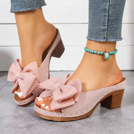 Kaelen rose pink textured fabric bow mule sandals with fish-mouth toe and 7cm block heel, worn by a model with blue denim jeans and a turquoise anklet.