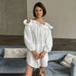 Model wearing a Kaelen white off-shoulder cotton mini dress with voluminous balloon sleeves, styled for a chic bohemian aesthetic in a relaxed interior setting.