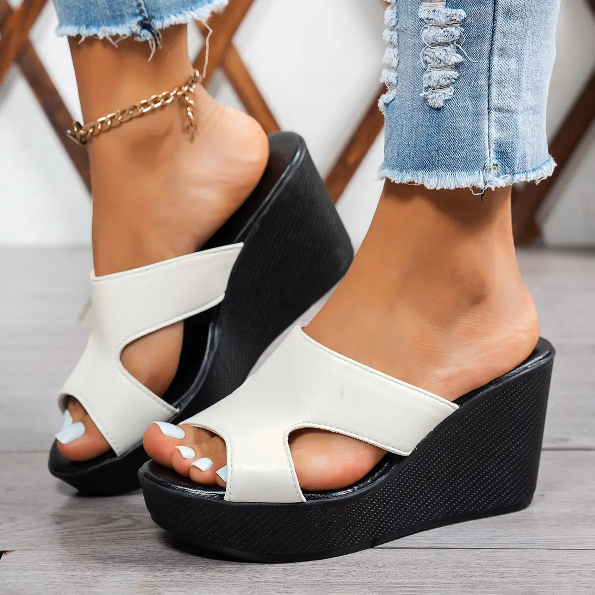 White Kaelen peep-toe wedge sandals with a single strap, styled with ripped denim jeans on a woman's feet, showcasing the comfortable platform heel.