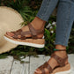 Brown Kaelen women's flat sandals with multi-strap design and knot detail, worn on feet with jeans and a straw hat nearby. Features hook-and-loop closure and a wood-grain effect platform sole.