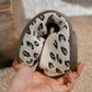 Close-up of Kaelen women's knit ballet flats showcasing the creamy off-white base with black and brown leopard print pattern and a flexible dark rubber sole held by hand.