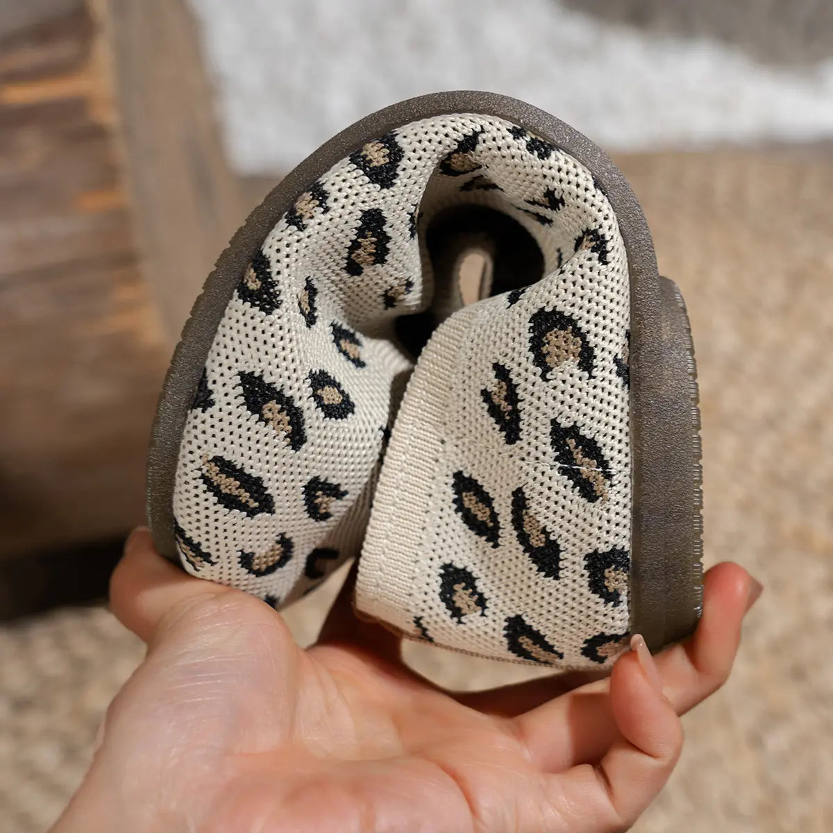 Close-up of Kaelen women's knit ballet flats showcasing the creamy off-white base with black and brown leopard print pattern and a flexible dark rubber sole held by hand.