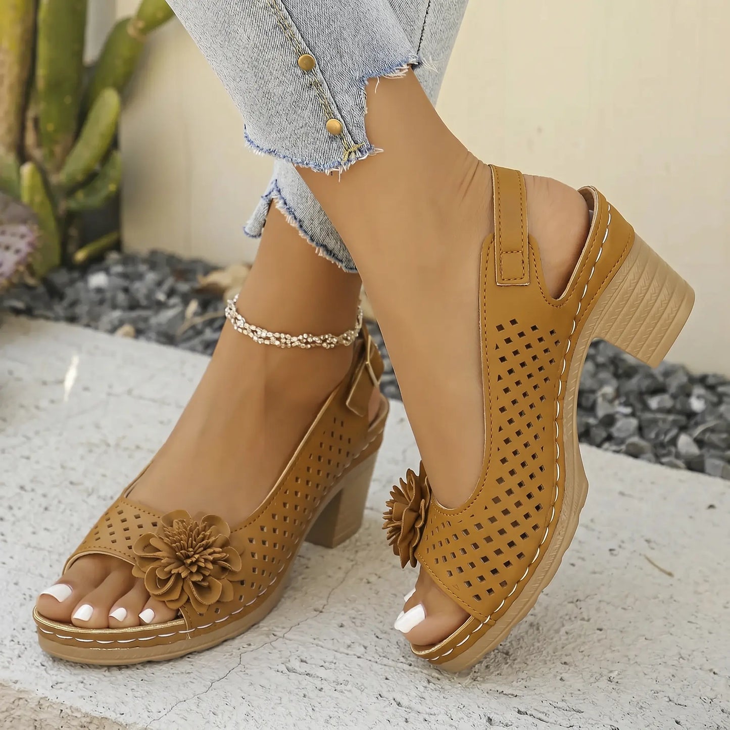 Kaelia Caramel Whisper chunky block heel sandals featuring a floral embellishment, perforated upper, and adjustable slingback strap, shown on a model's feet with white toenails.