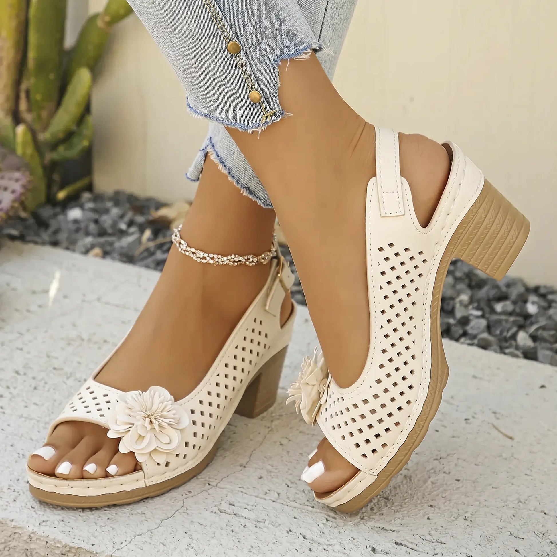Woman's feet wearing Kaelia Pure Ivory peep-toe chunky heel sandals adorned with a floral embellishment and perforated square pattern, styled with distressed jeans.