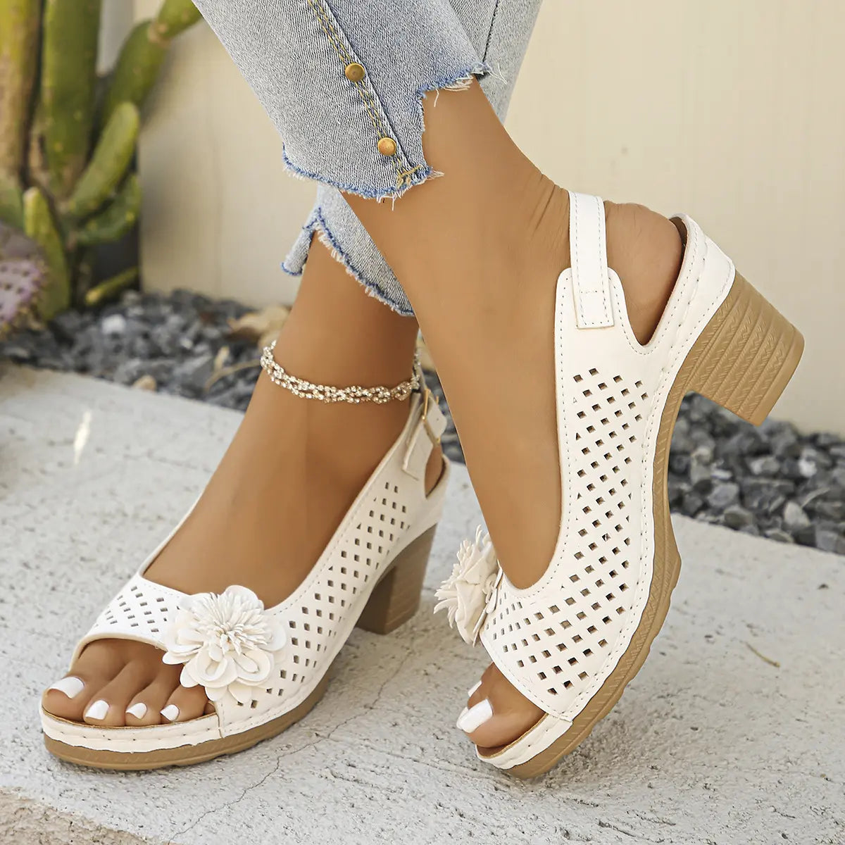 White Kaelia peep-toe chunky heel sandals with floral embellishment and perforated upper, shown on a woman's feet with light-wash jeans and an anklet.