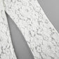 Close-up view of Kaelia white lace flared trousers showcasing intricate floral jacquard texture and sheer fabric construction. The wide leg silhouette is partially visible.