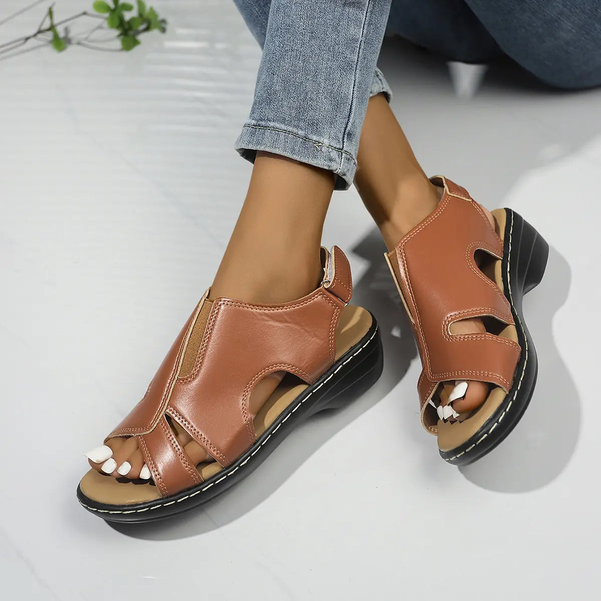 Kaelin women's brown faux leather peep-toe wedge sandals with white contrast stitching and adjustable ankle strap, shown on a model with jeans. These comfortable summer shoes offer elegant style and all-day wearability.