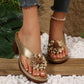 Gold Kaelis women's slide sandals featuring a large 3D floral embellishment and chunky block heel, styled with distressed denim in a bohemian setting with wood and pebbles.