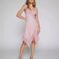 A Kaelis pink lace V-neck midi dress with cascading ruffles and an asymmetrical tiered hem, shown on a model in a studio. The sleeveless design features delicate ruffled shoulder straps.