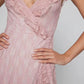 A woman wearing a Kaelis pink lace V-neck midi dress with cascading ruffles and an asymmetrical tiered ruffle hem, shown from the torso down with hands on hips.