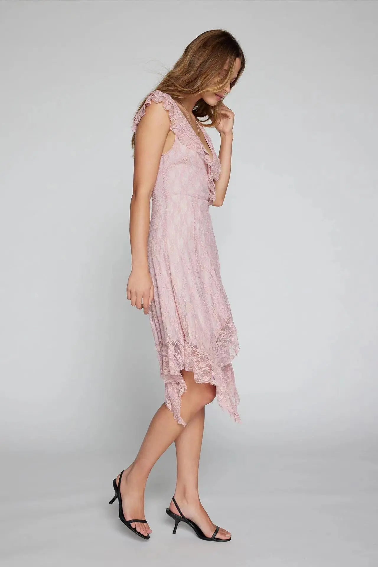 Woman in a flowing pink Kaelis lace midi dress featuring a V-neck with cascading ruffles and an asymmetrical tiered ruffle hem. This bohemian-chic style is shown in profile.