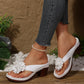 Women's white Kaelis floral platform slide sandals on a model's feet, showcasing the 3D flower embellishment, chunky wood-effect heel, and layered sole against a lifestyle background.