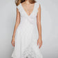 Kaelis romantic white lace V-neck midi dress with cascading ruffles and an asymmetrical tiered ruffle hem, shown on a model with a slight three-quarter view.