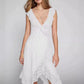 Kaelis white lace V-neck midi dress with cascading ruffles and an asymmetrical tiered ruffle hem, shown on a model with a studio background.