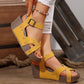 Yellow Kaelix wedge sandals with studded criss-cross straps worn by a model with ripped white jeans and a colorful beaded anklet on a wooden floor.