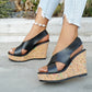 Black faux leather Kaelo wedge sandals with criss-cross straps and a multi-color flecked cork wedge, shown on a model's feet in a natural outdoor setting.