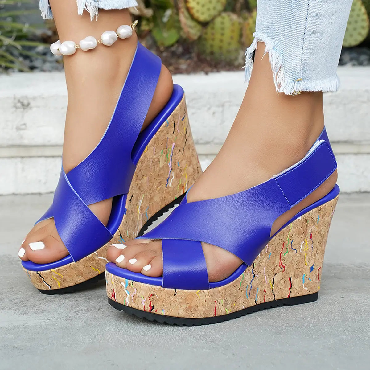 Model's feet wearing Kaelo blue wedge sandals with criss-cross straps and a multi-colored speckled cork platform and wedge, styled with distressed denim.
