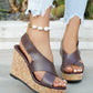 Kaelo dark brown faux leather wedge sandals with criss-cross straps and multi-color speckled cork platform, shown on a model's feet in a natural outdoor setting.