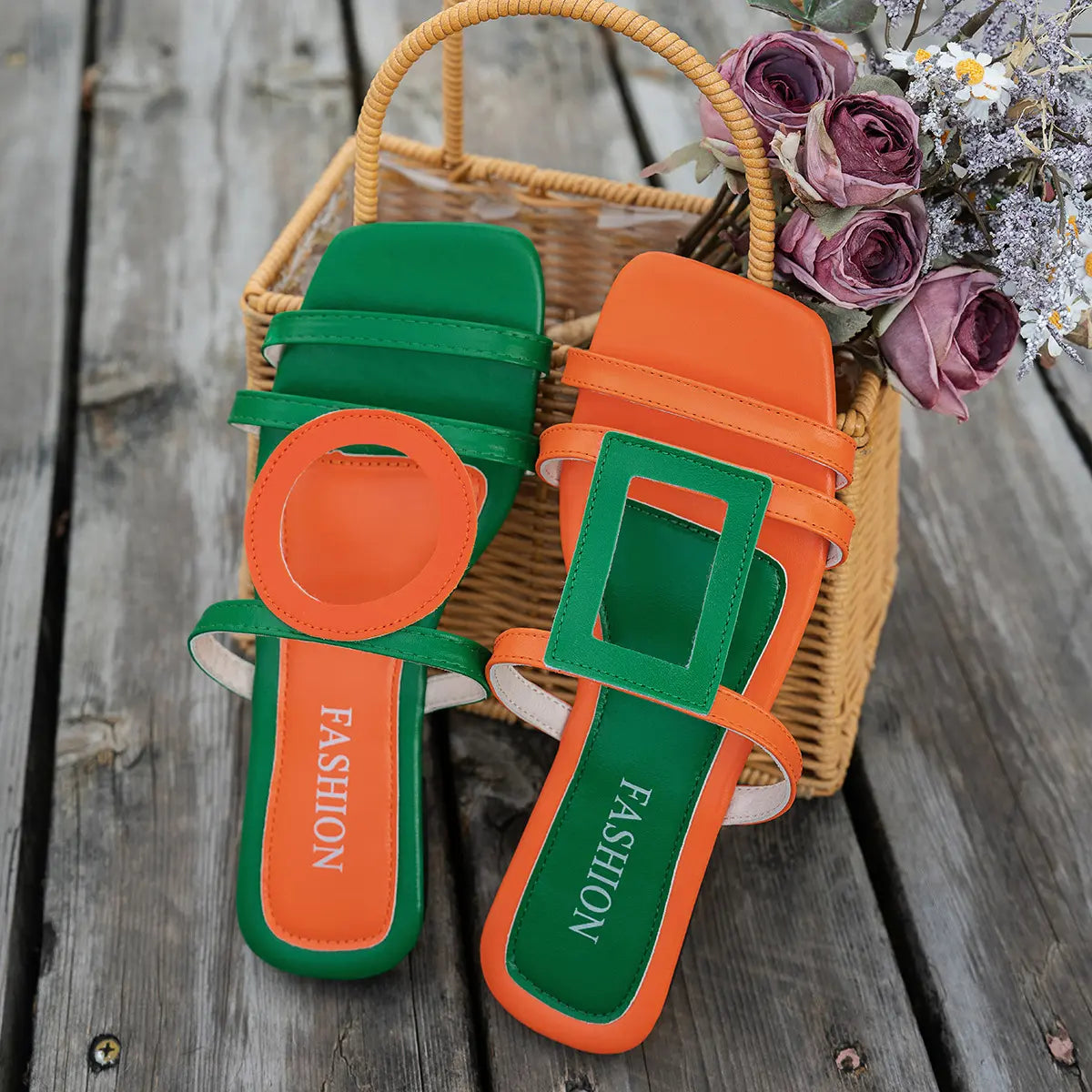 Kaelo orange and green color block flat sandals with geometric and circular accents, displayed in a woven basket with dried flowers on a wooden surface.