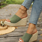 Olive green knitted espadrille wedge sandals with a thick jute-wrapped platform sole are showcased on a woman's feet, styled with casual blue jeans on a wooden boardwalk.