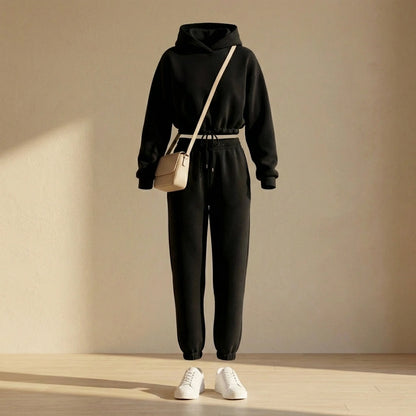 Kaelo women's cropped hoodie and jogger set in black fleece, front view styled with a beige crossbody bag and white sneakers.