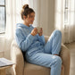 Kaelo women's cropped hoodie and jogger set in light blue fleece, worn by a model sitting in a beige armchair.