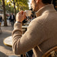 Kaelon mens ribbed zip cardigan in beige, lifestyle side view showing the architectural knit texture and stand collar while worn at a cafe.
