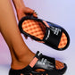 Black Kaelos comfort slide sandal with coral accents, worn on a foot, featuring embossed 'FASHION LIFE IS BEAUTIFUL' text on the strap and a textured orange footbed.