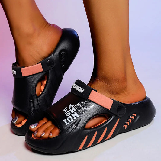 Black Kaelos comfort slides for women, featuring coral accents and embossed 'FASHION LIFE IS BEAUTIFUL' text on the strap, shown on feet from a three-quarter angle against a soft gradient studio background.