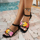 Kaelos women's black flat sandals featuring vibrant multi-colored heart embellishments on the front strap and a black elasticated ankle strap, styled on feet with an anklet against a tiled and blurred water background.