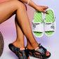 Lifestyle image showcasing Kaelos comfort slide sandals in black and white variants, featuring embossed 'FASHION' and 'LIFE IS BEAUTIFUL' text on the straps, coral and lime green accents, and textured footbeds.