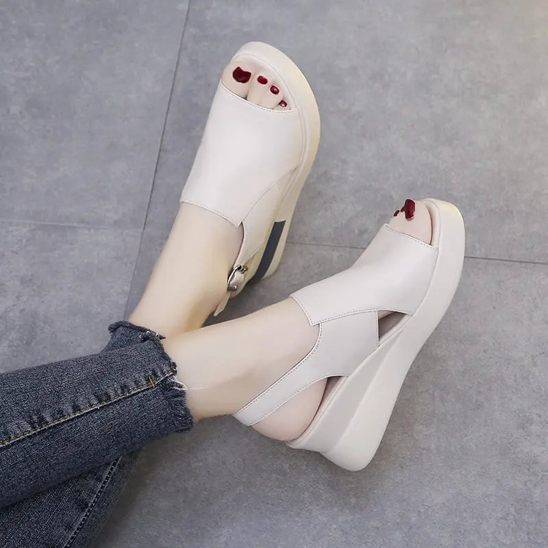 A pair of creamy off-white Kaelos wedge sandals with a fish mouth peep-toe, crossover straps, and adjustable slingback buckle are worn by a model with distressed denim jeans.