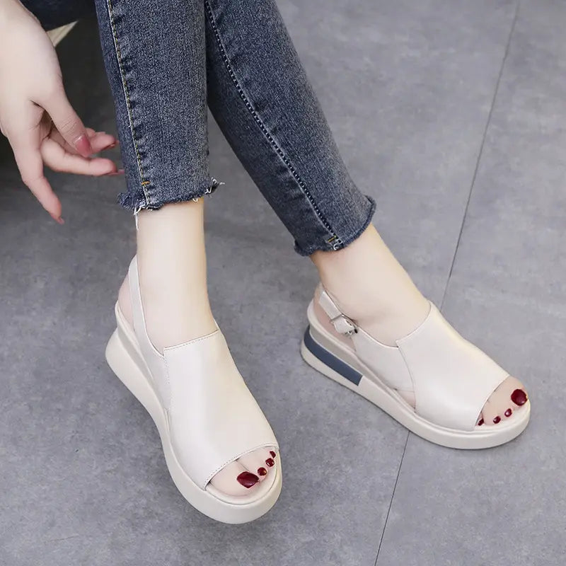 Creamy off-white Kaelos wedge sandals with a crossover peep-toe and adjustable slingback strap, shown worn with denim jeans.