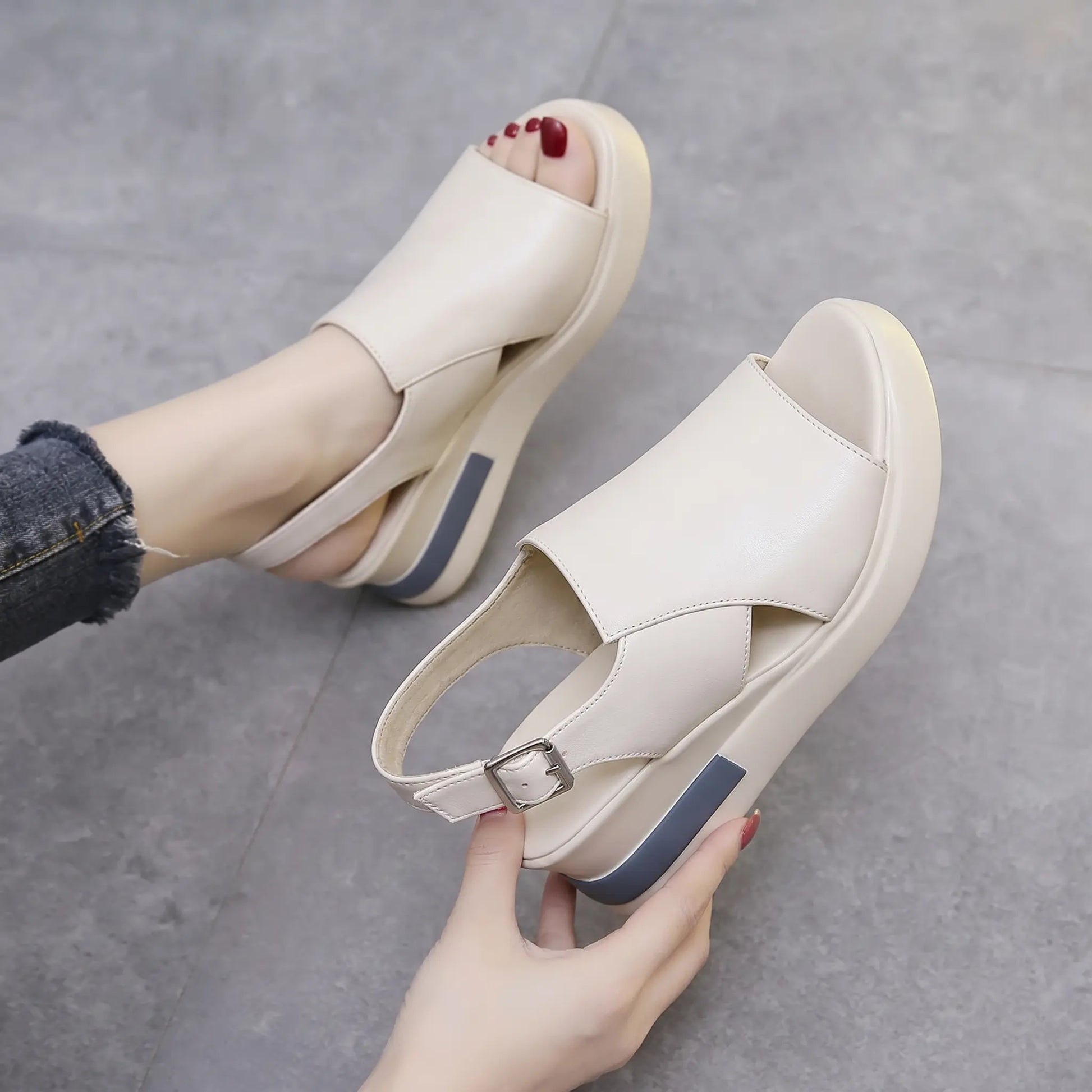 A pair of Kaelos creamy off-white wedge sandals shown from a three-quarter angle, featuring a crossover peep-toe vamp and adjustable slingback strap, with a grey accent stripe on the wedge.