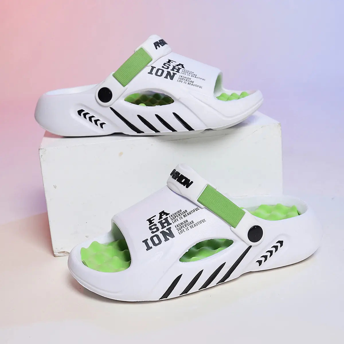 White Kaelos comfort slides with lime green straps and soles, featuring embossed 'FASHION' and 'LIFE IS BEAUTIFUL' text and black side graphics. This image shows a three-quarter view of the sandals placed on a prop.