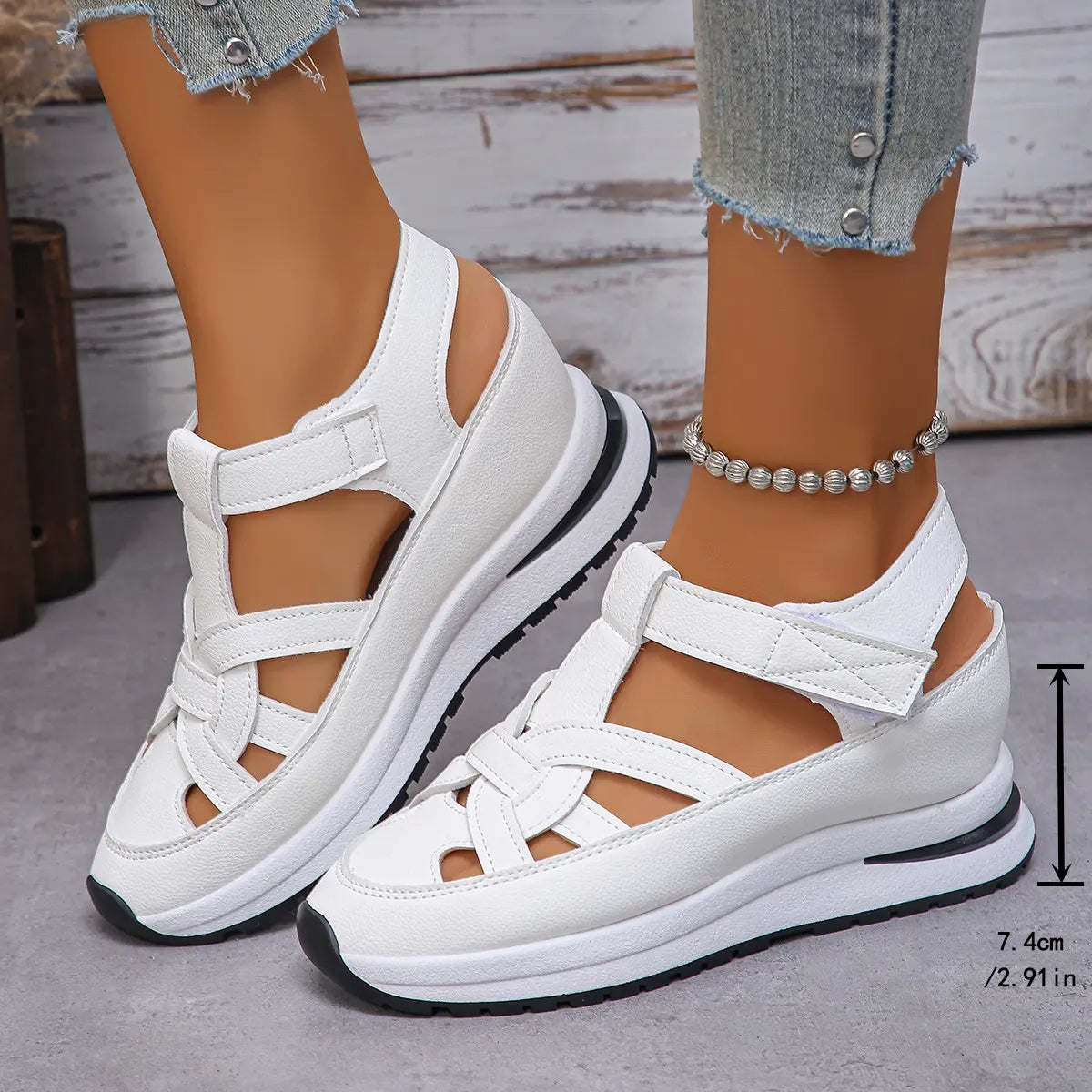 White Kaelum platform wedge sandals featuring a closed round toe and three overlapping cut-out straps with hook-and-loop closures, shown on feet with jeans and an anklet. A side measurement overlay indicates 7.4cm height.