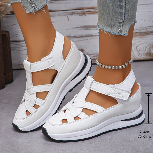 White Kaelum platform wedge sandals featuring a closed round toe and three overlapping cut-out straps with hook-and-loop closures, shown on feet with jeans and an anklet. A side measurement overlay indicates 7.4cm height.