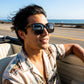 KAEON oversized square sunglasses in black worn by a man driving a convertible along the coast, showing the thick architectural frame and metal temple accents.