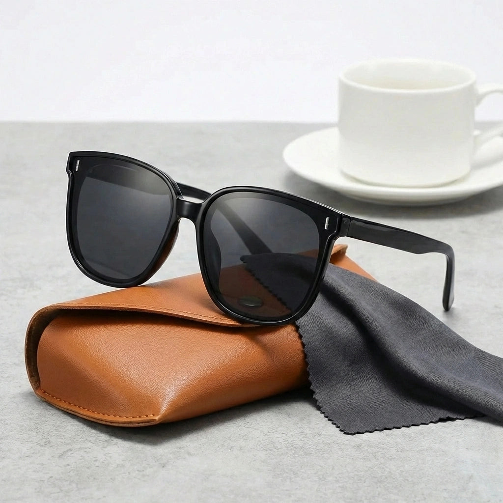 KAEON oversized square sunglasses in black with chunky architectural frame and UV400 lenses, resting on a brown case with cleaning cloth.