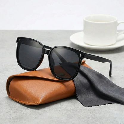KAEON oversized square sunglasses in black with chunky architectural frame and UV400 lenses, resting on a brown case with cleaning cloth.