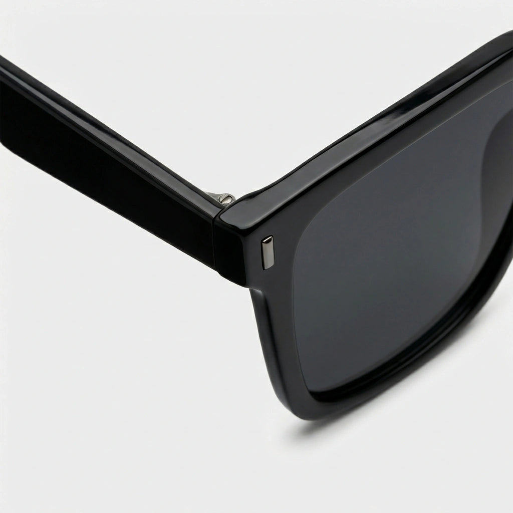 KAEON oversized square sunglasses in black, close-up view showing reinforced alloy hinge and signature metal temple accent.