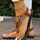 Bohemian brown flat sandals featuring a T-strap adorned with multicolor beads and golden mandala charms, with a braided elastic ankle strap, worn on a wooden deck. These artisanal sandals offer vibrant ethnic style and comfortable wear for summer.